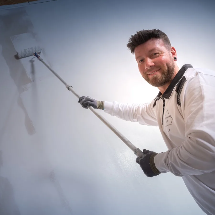 Andy Hansen streicht lächelnd eine Wand mit der Farbrolle